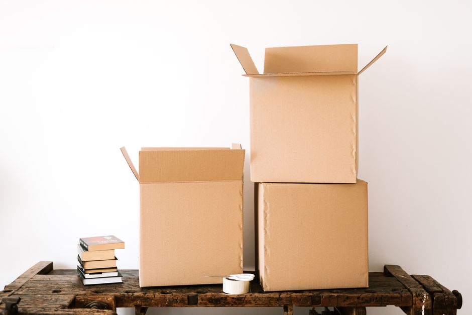 A neat stack of cardboard moving boxes sits in the corner of a bright, sunlit, and empty room, symbolizing an organized and controlled approach to selling a home.