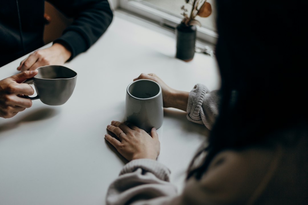 Two diverse individuals sit in a warm, inviting coffee shop, having a supportive conversation that represents open financial communication and seeking community help.